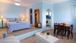 Ein Schlafzimmer mit einem Bett, Nachttischlampen, einem Nachttisch mit einem Buch und einer Pflanze, einem Holzstuhl und einem Esstisch mit Stühlen.