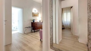 Une pièce avec un plancher en bois, une commode, un miroir et une porte donnant sur une autre pièce.