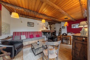 Ein rustikales Interieur mit Holzbalkendecke, einer Couch, einem Esstisch und einem Kamin.