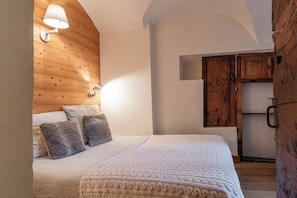 Un dormitorio con cabecera de madera, cama con cubrecama blanco, dos almohadas mullidas, lámpara de pared y un mueble de madera.