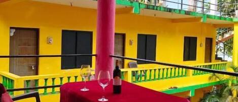 A balcony with a table and chairs, a view of a yellow building, and a palm tree in the background.