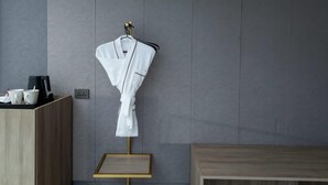 A white bathrobe hanging on a wooden hanger against a grey textured wall. - Ramada Encore by Wyndham Boracay White Beach (Boracay Island)