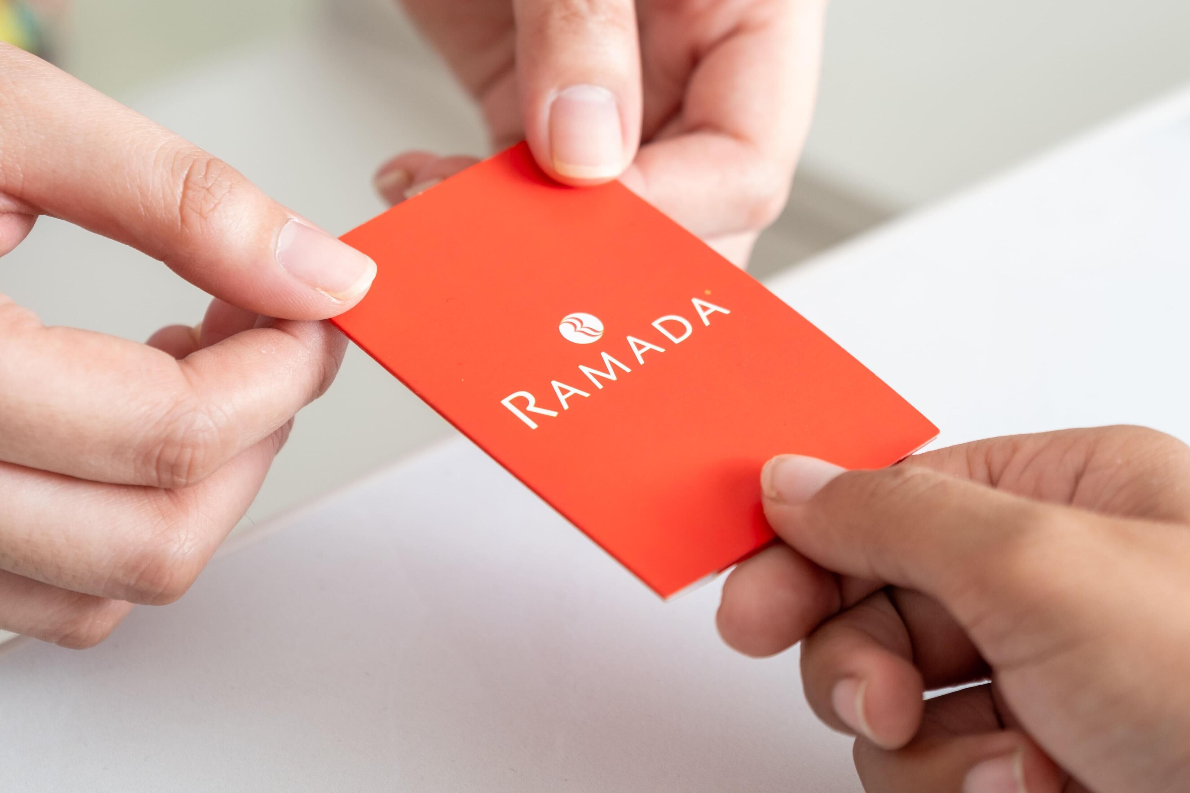Eine Person übergibt eine rote Karte mit dem Schriftzug 'RAMADA' an eine andere Person.