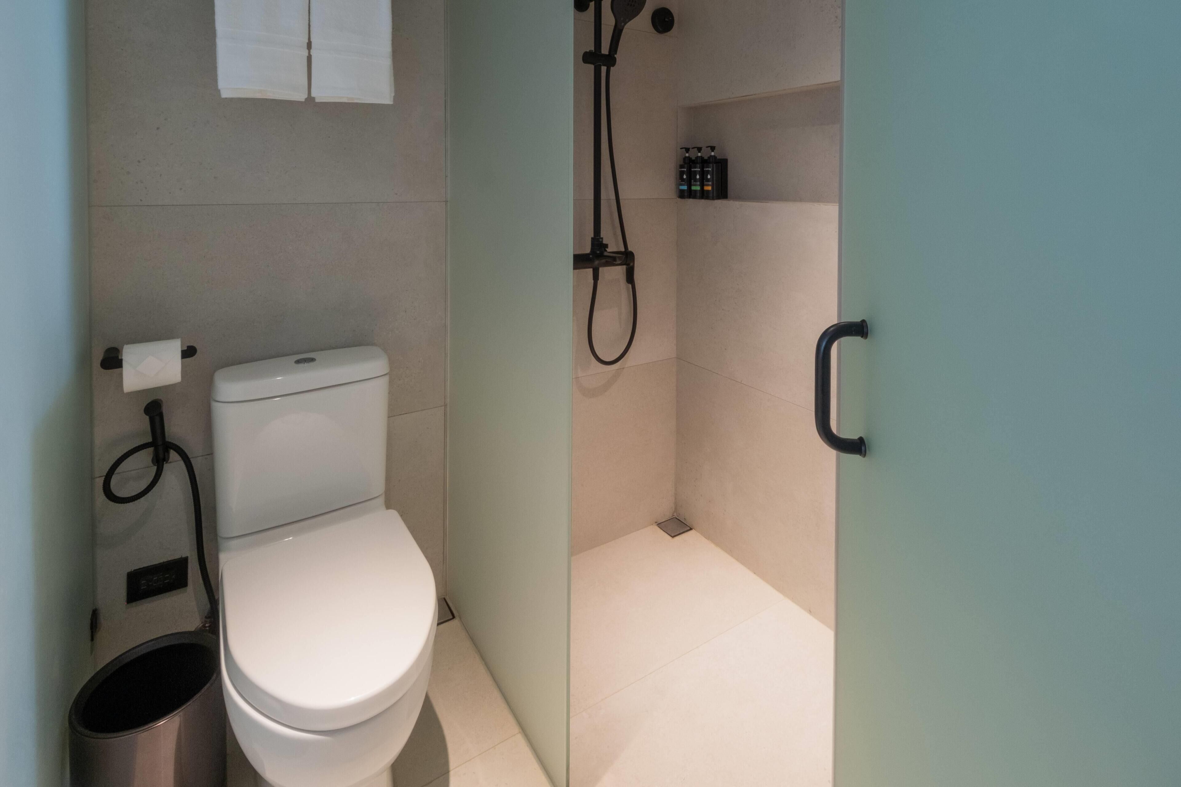 A compact bathroom with a toilet, a shower, and a toilet paper holder.