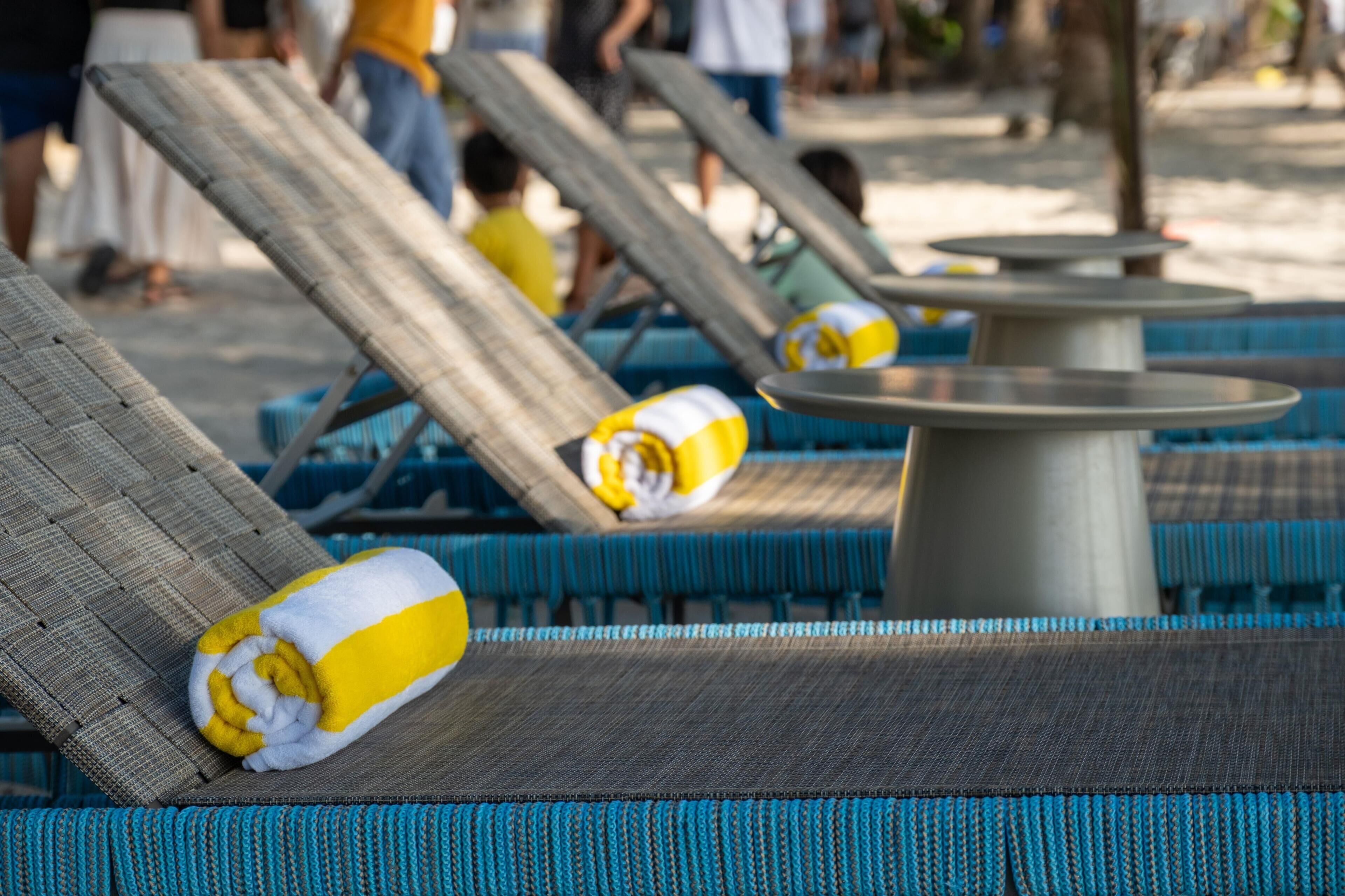 A row of lounge chairs with towels, a round table, and a poolside setting.