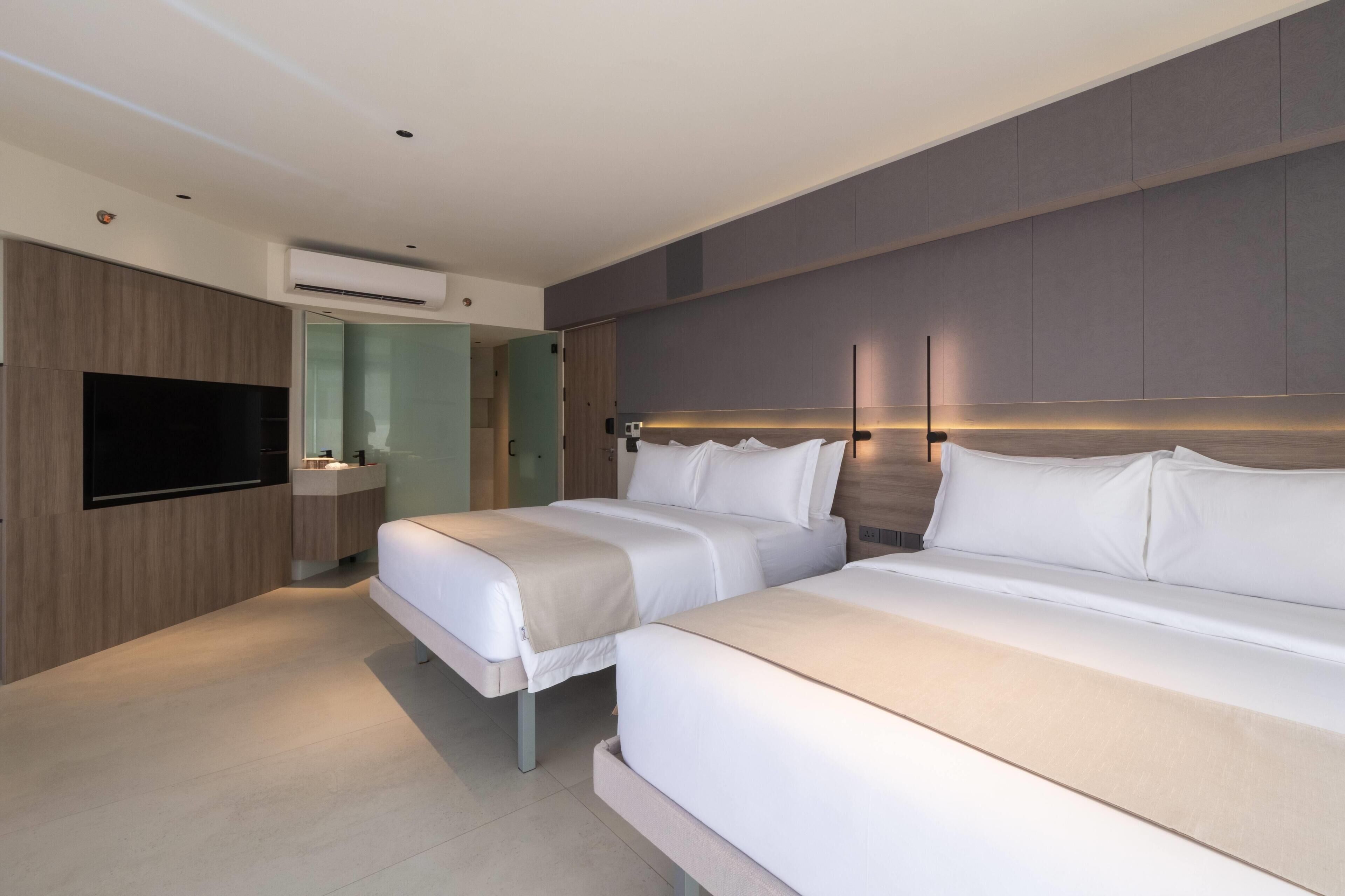 Een moderne hotelkamer met twee bedden, een flatscreen televisie, een kaptafel met spiegel en een airconditioner.