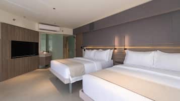 A modern hotel room with two beds, a flat-screen TV, a vanity with a mirror, and an air conditioning unit.