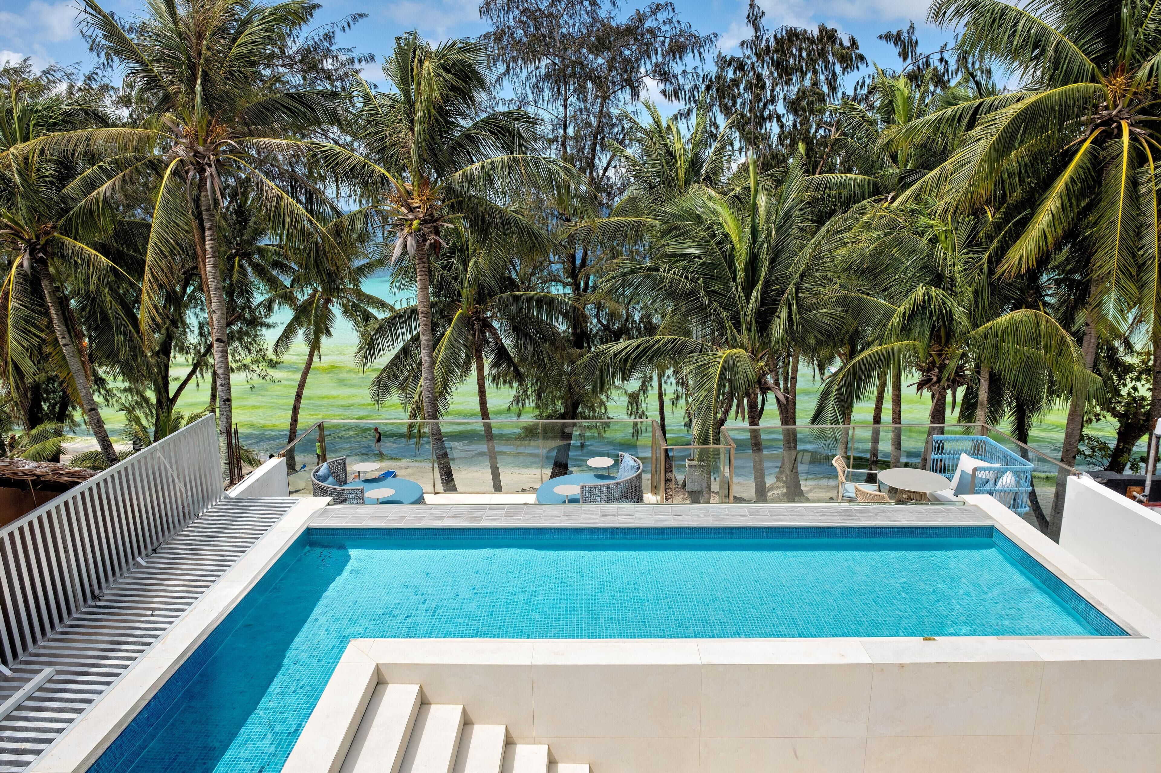 A pool with clear blue water, surrounded by palm trees and a view of the ocean.
