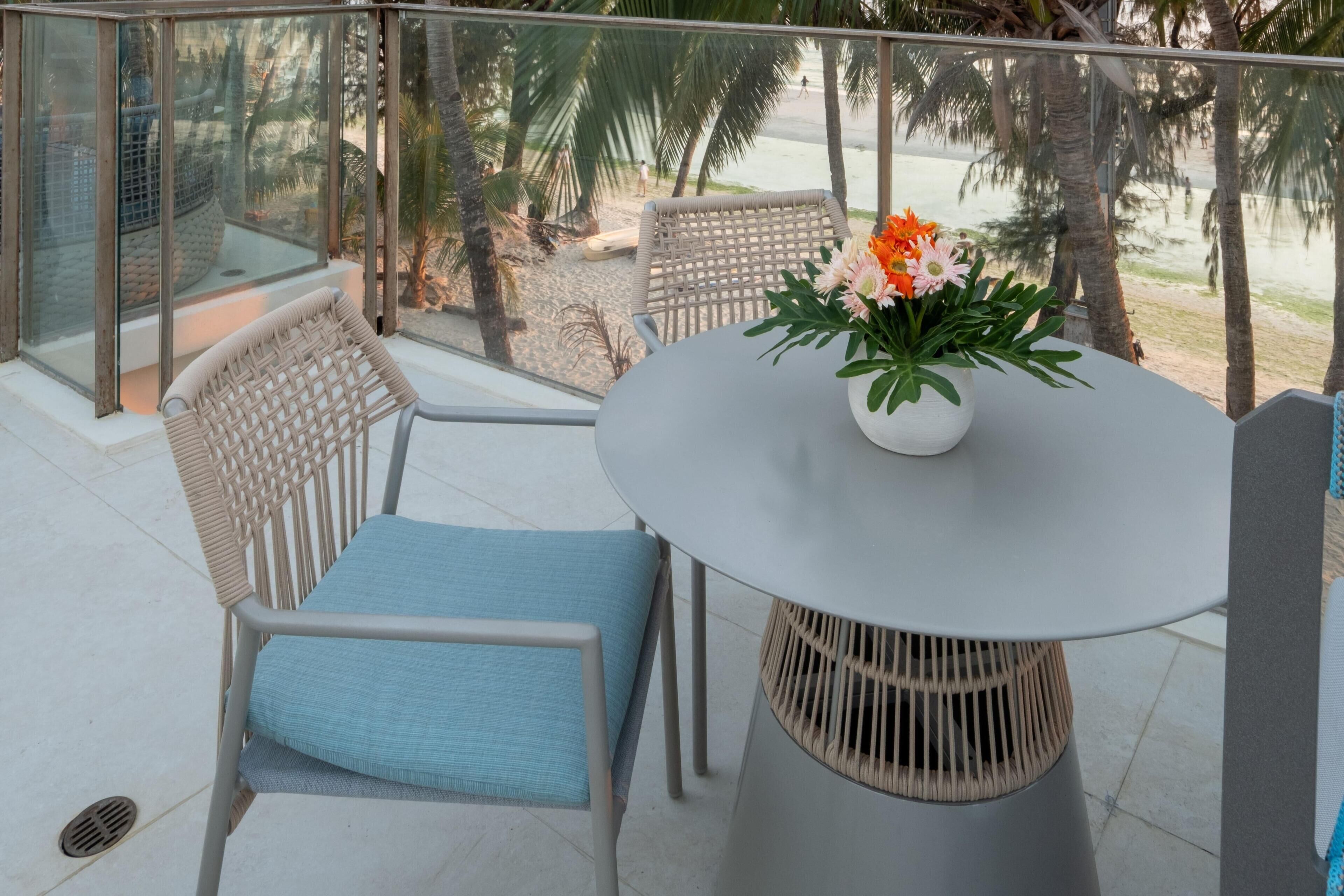 A balcony with a round table and two wicker chairs, one with a blue cushion.