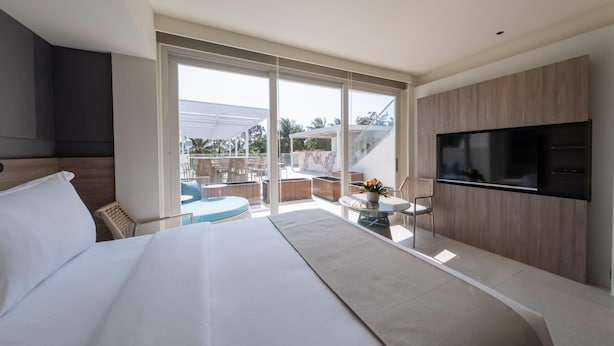 A modern hotel room with a large bed, a flat-screen TV, and a balcony with outdoor seating. - Ramada Encore by Wyndham Boracay White Beach (Boracay Island)