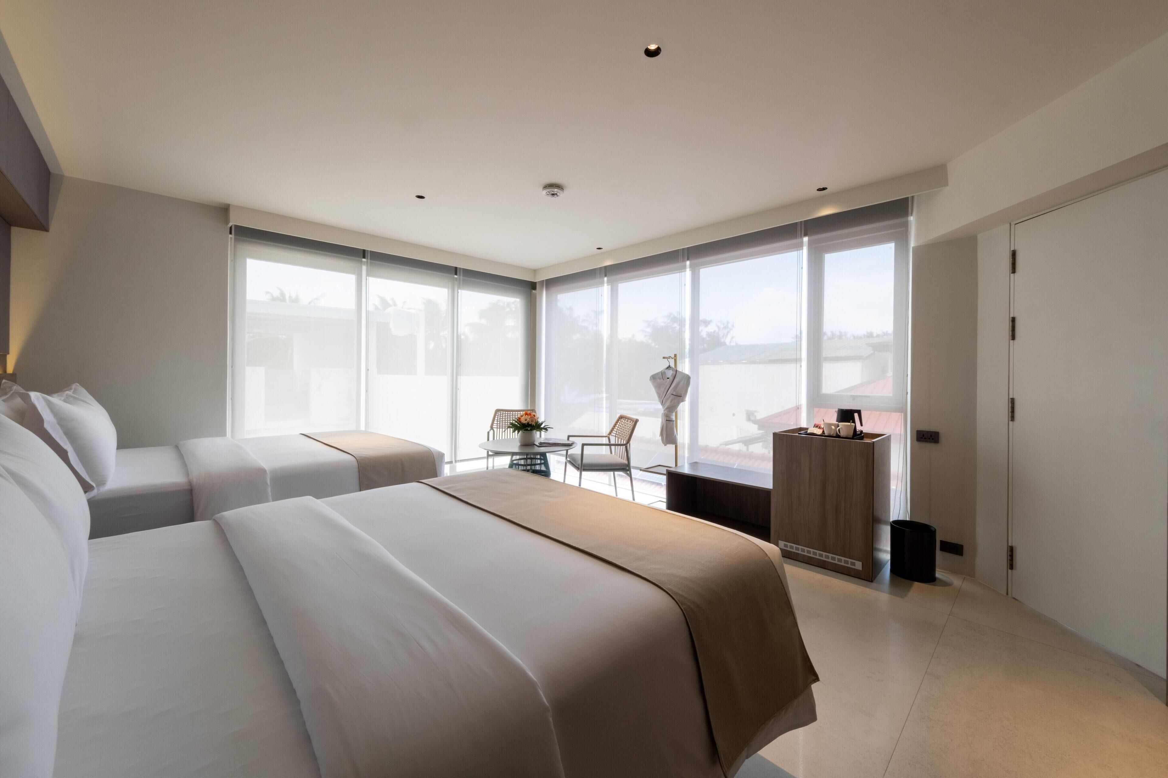 Une chambre d’hôtel moderne avec deux lits, une petite table avec des chaises, un bureau et de grandes fenêtres.