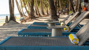A beachside lounge area with wicker lounge chairs and a central table, surrounded by palm trees and a view of the ocean. - Ramada Encore by Wyndham Boracay White Beach (Boracay Island)