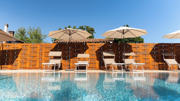 A swimming pool with lounge chairs and umbrellas, surrounded by a brick wall. - Elegant House with Swimming Pool and Large Green Garden (Veneto)
