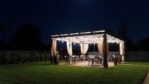A covered outdoor patio with tables and chairs, a wooden pergola, and a moon in the sky. - Elegant House with Swimming Pool and Large Green Garden (Veneto)