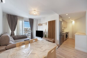 A modern living room with a sofa, a dining table, a TV, and a kitchen area with a refrigerator and washing machine. - Apartment 'En Benalmádena 402' with Sea Views, Wi-Fi and Air Conditioning (Benalmádena)