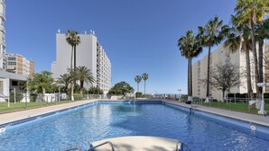 Una piscina con acqua cristallina, circondata da palme e un alto edificio sullo sfondo.