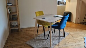 Ruokailutila, jossa on pöytä, tuoleja, puulattia, kirjahylly ja taustalla keittiö.