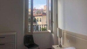A room with a large window, a chair, a bedside table with a lamp, and a dresser. - Bsddfffffffff (Firenze)