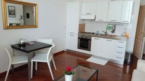 A compact kitchen with white cabinets, a dining table with chairs, and a small table with a potted plant. - Bsddfffffffff (Firenze)