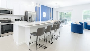 A modern kitchen with a central island, bar stools, and a blue accent wall. - Affordable Stays Kissimmee (Kissimmee)