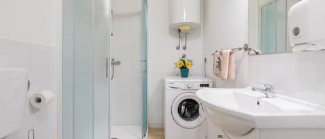 A modern bathroom with a glass shower enclosure, a washing machine, and a sink with a mirror.