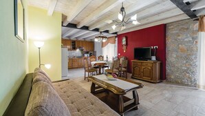 Ein Wohnzimmer mit einer Couch, einem Esstisch mit Stühlen, einer Küche im Hintergrund und einer Steinwand.