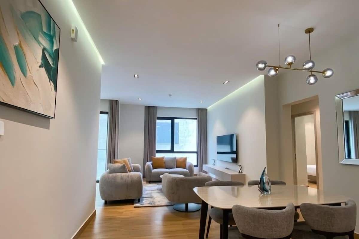 A modern living room with a dining area, a sofa set, a flat-screen TV, and a painting on the wall.