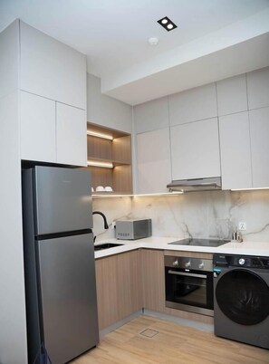 A modern kitchen with a stainless steel refrigerator, built-in microwave, oven, and washing machine.