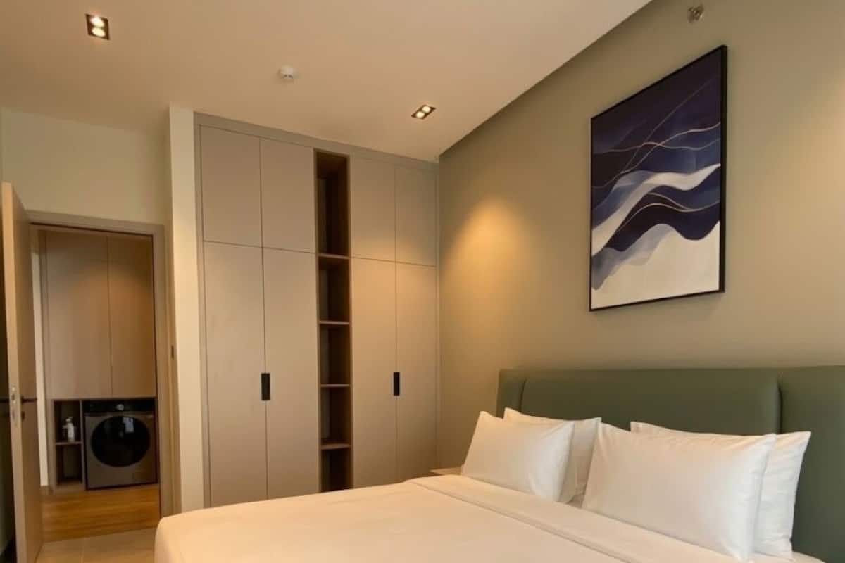 A modern bedroom with a large bed, built-in wardrobe, and a wall-mounted artwork.