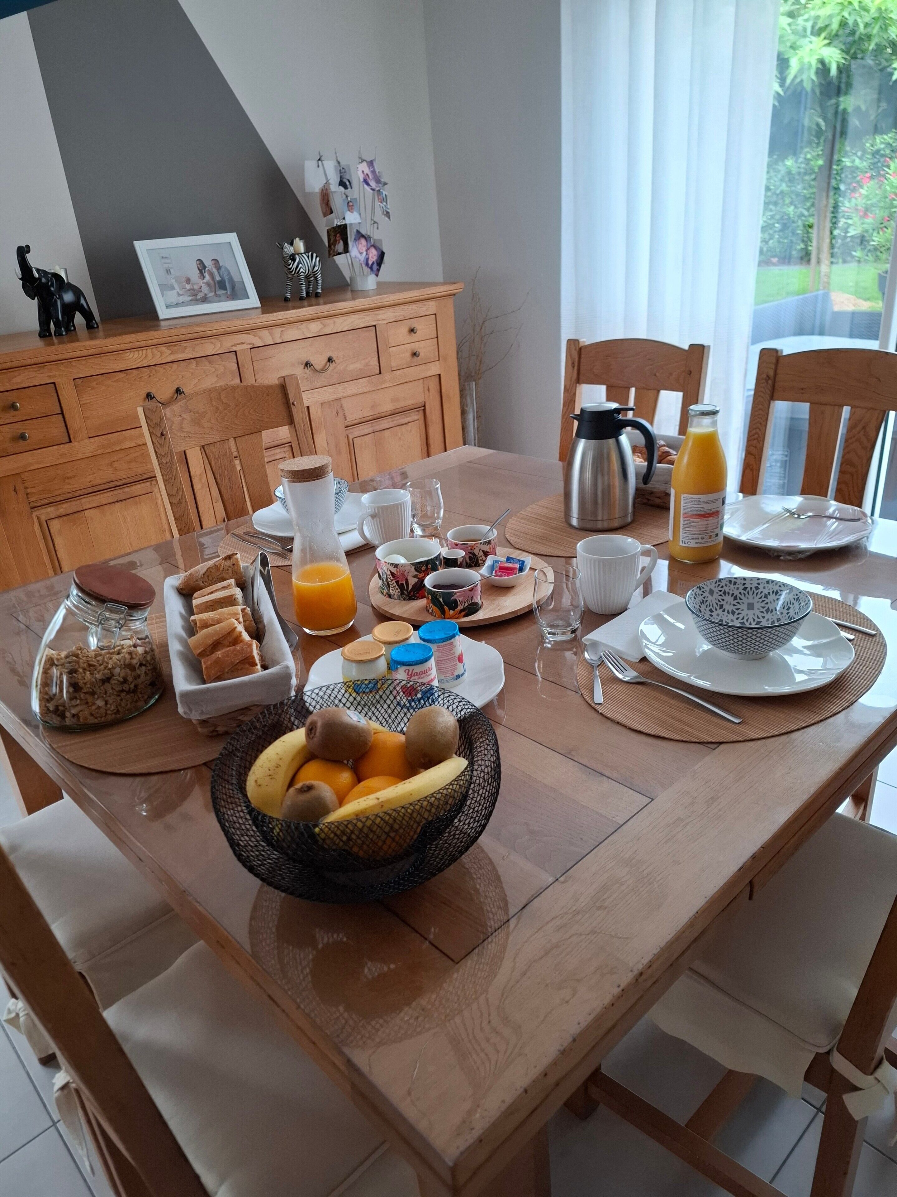 Desayuno con una mesa de madera, diferentes alimentos, una cafetera y vistas al exterior.