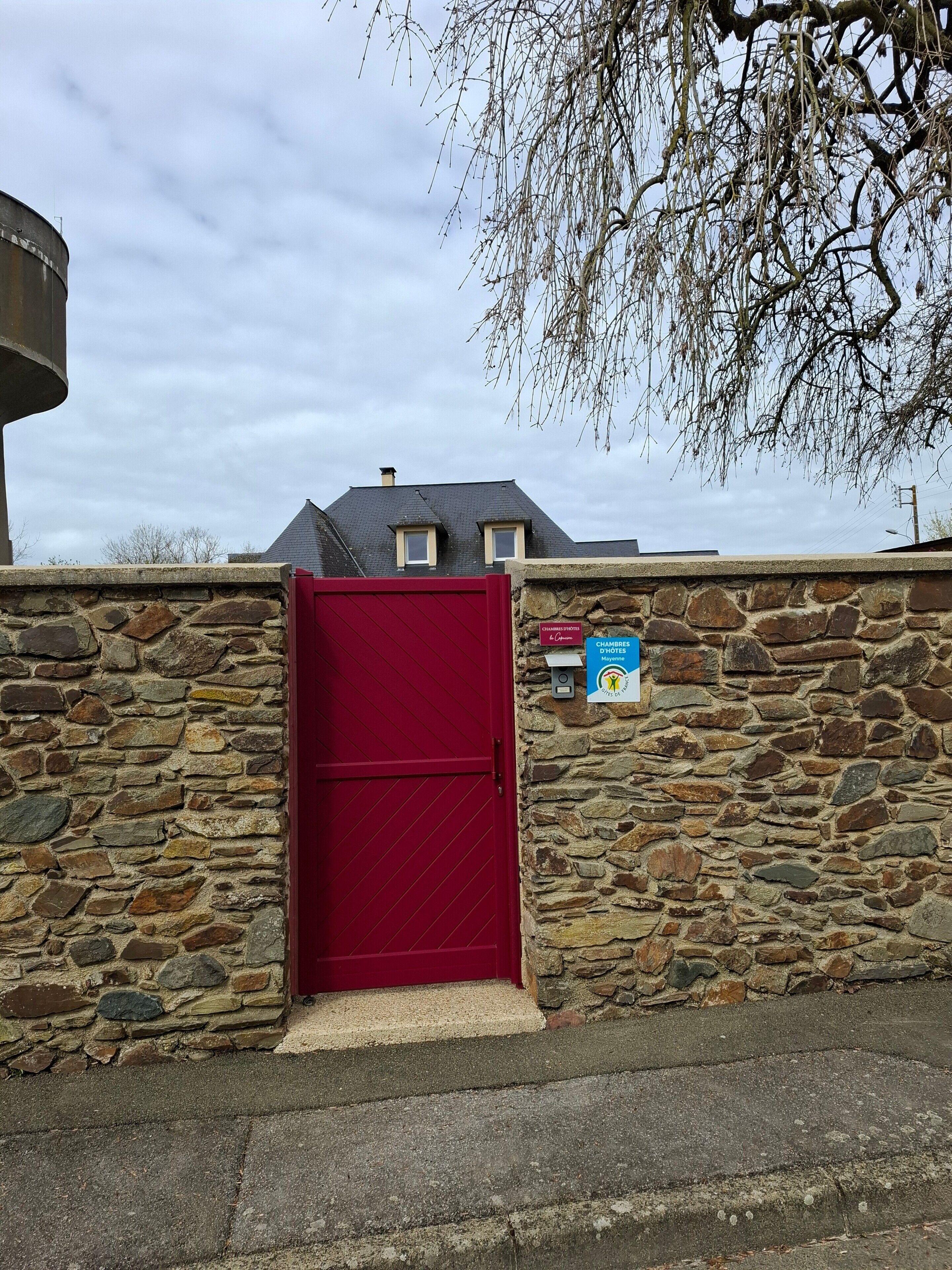 A stone wall with a red door, a mailbox, and a house in the background.