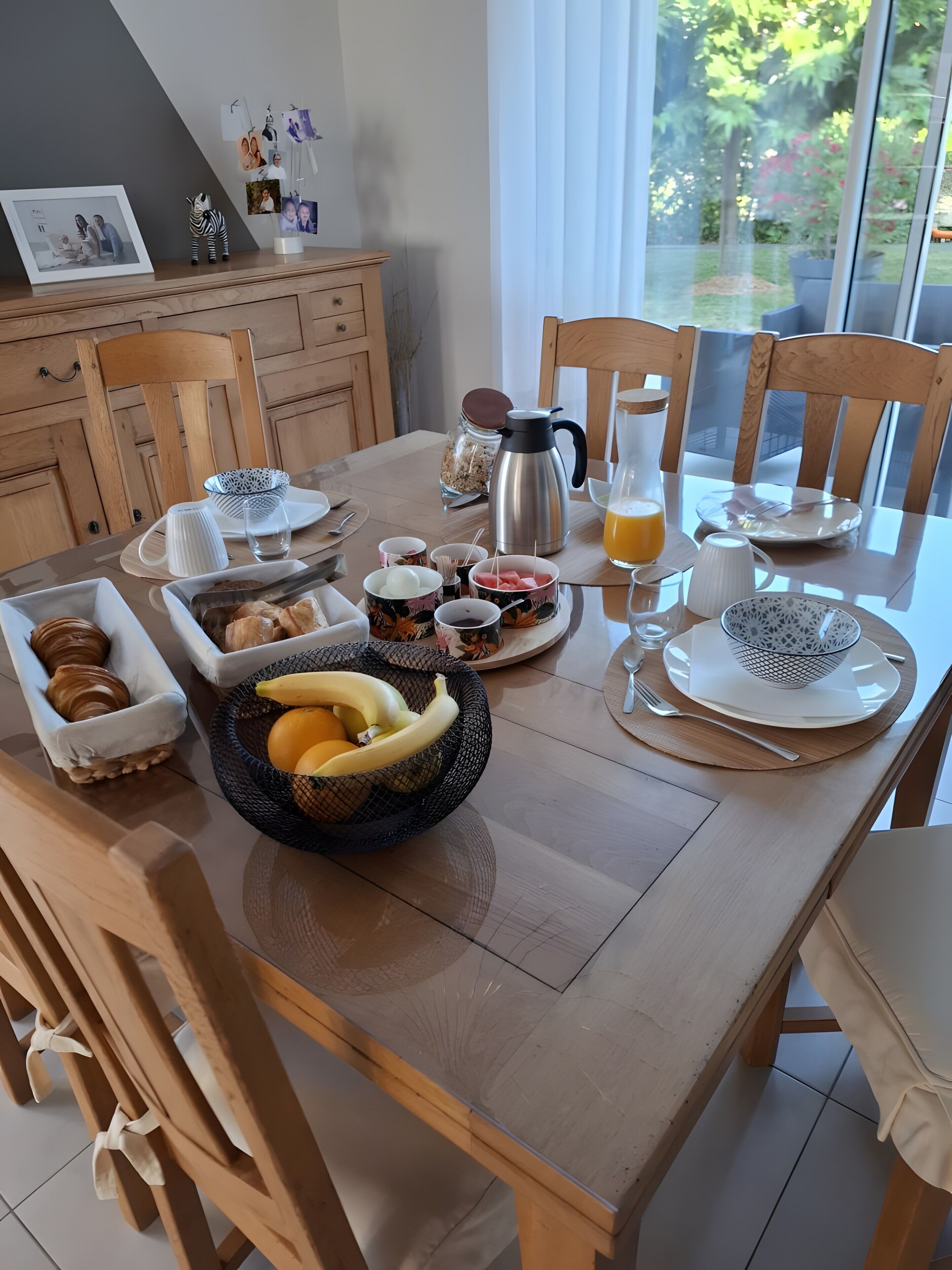 Una colazione con tavolo di legno, sedie, una moka, frutta e vista sul verde.