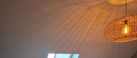 Ein modernes Loft-Schlafzimmer mit Dachfenster, einer kleinen Küchenzeile, einem Sofa und einem runden Tisch.