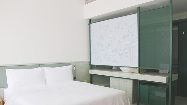 Una habitación de hotel con una cama, una pizarra con diagramas, un armario verde y una pared con azulejos.