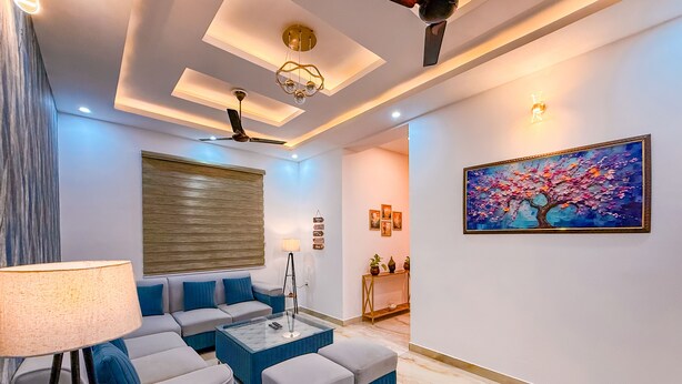 Ein modernes Wohnzimmer mit Sofa, Hocker, Couchtisch, Stehlampe, Deckenventilator und Kunstwerk an der Wand.