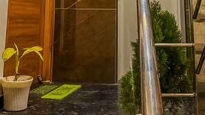 Ein Hotel Eingang mit einer Holztür, einem Schild mit der Aufschrift 'BLUE HEAVEN', einem Schild für die erste Etage, einer Metalltreppe und Topfpflanzen.