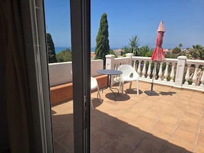 Ein Balkon mit Tisch und Stühlen, einem roten Sonnenschirm und Blick aufs Meer.