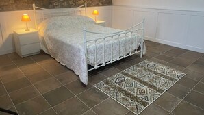 Un dormitorio con pared de piedra, cama blanca con colcha estampada, dos lámparas de noche y una alfombra con diseño.