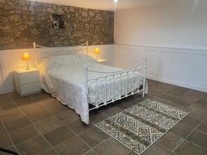 Ein Schlafzimmer mit einer Steinwand, einem weißen Bett mit gemustertem Überwurf, zwei Nachttischlampen und einem gemusterten Teppich.