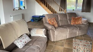 Una sala de estar con sofá, mesa de centro, alfombra estampada, ventana con cortinas y una escalera.