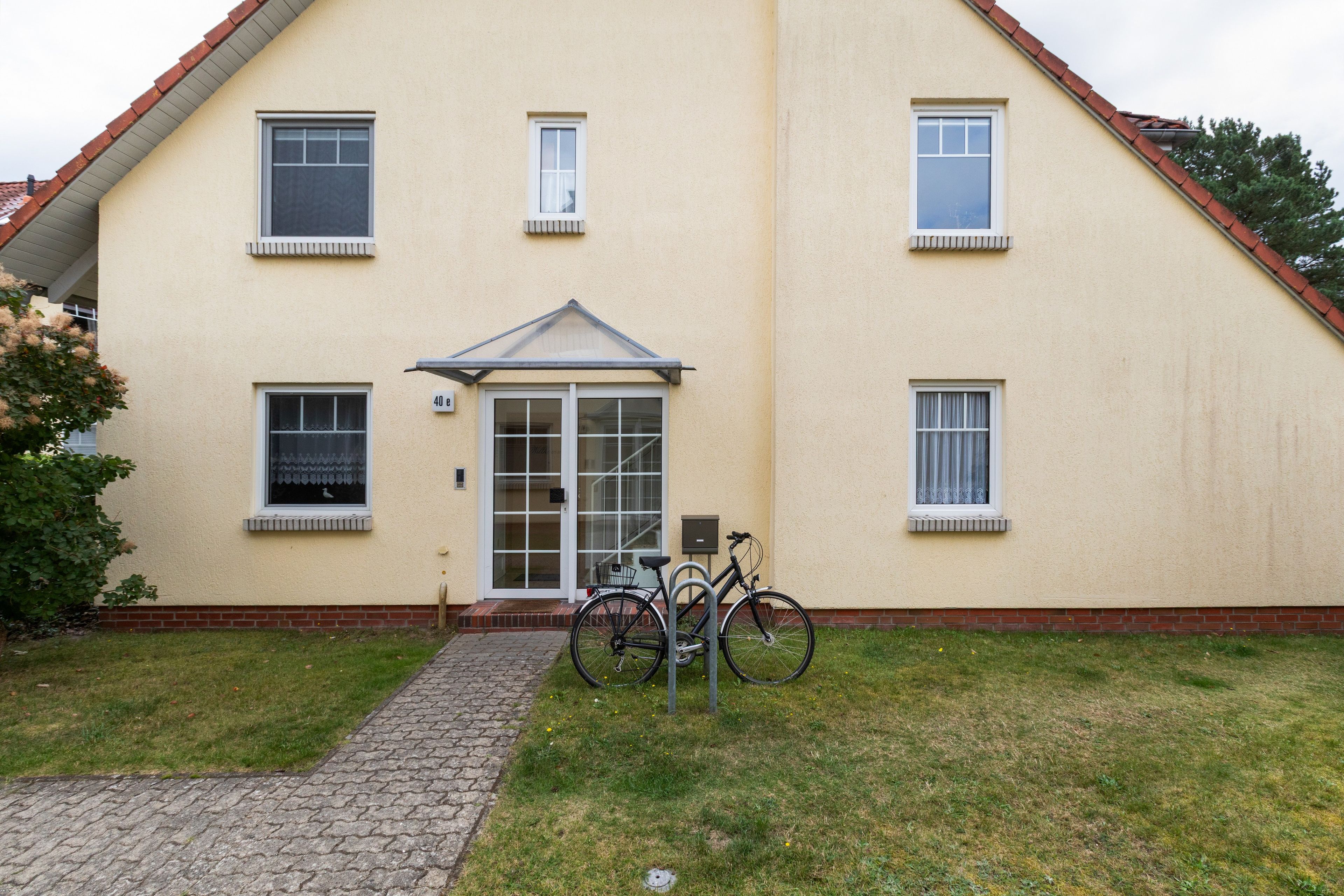 Ein zweistöckiges Gebäude mit einem zentralen Eingang, einer Veranda und einem Fahrrad davor.
