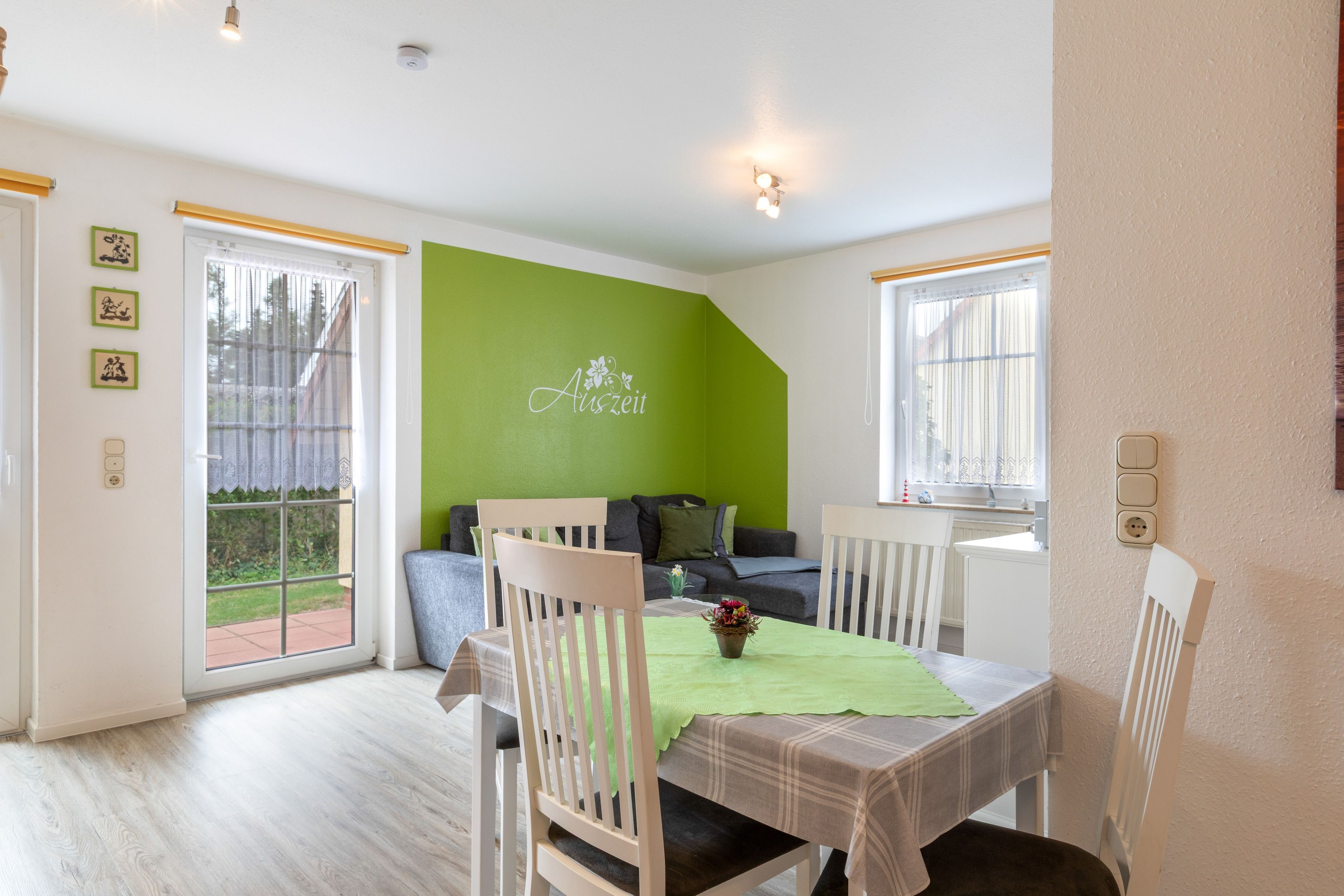 A dining area with a table set for two, a green accent wall, and a sofa in the background.