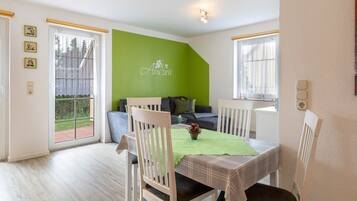 A dining area with a table set for two, a green accent wall, and a sofa in the background.