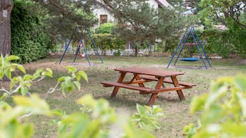 Et picnicbord i en græsplæne med gynger og en bygning i baggrunden.