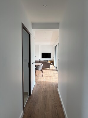A modern hallway with a wooden floor, a flat-screen TV mounted on the wall, and a sofa in the background. - Apartment with terrace - Near sea and center (Royan)