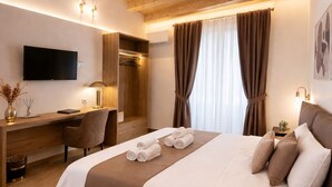 A hotel room with a large bed, a desk, a chair, a TV, and a window with curtains. - Sicily Luxury Suites (Palermo)