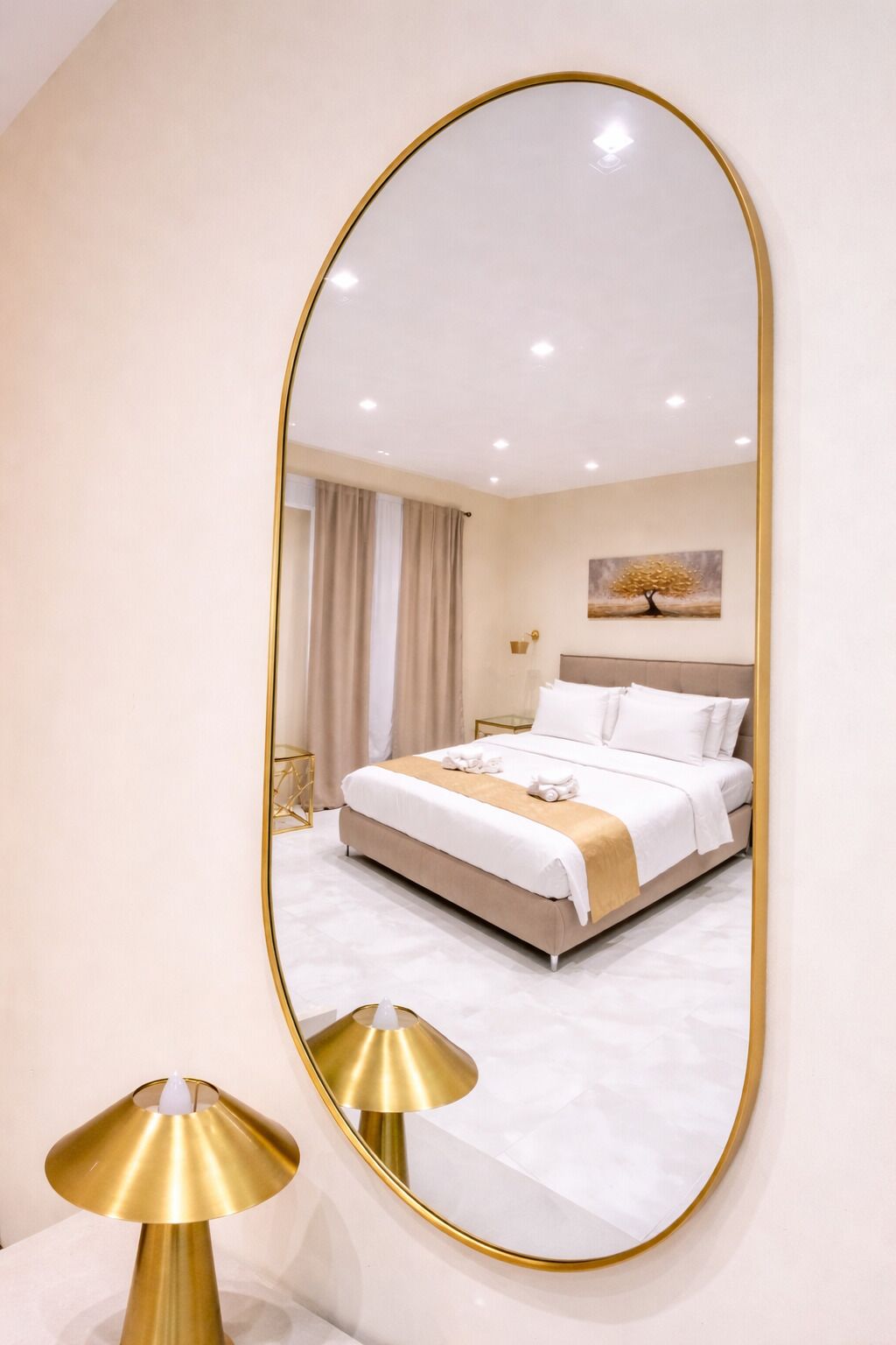 A bedroom with a bed, a bedside table, a lamp, and a wall-mounted mirror.