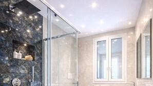 A modern bathroom with a glass-enclosed shower, a freestanding bathtub, a vanity with a mirror, and a marble-tiled floor. - Sicily Luxury Suites (Palermo)