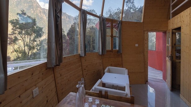 Una baita di legno con ampie finestre, un tavolo con bicchieri e tazze, e vista sulle montagne.