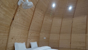 Una stanza con soffitto a falde, pareti in legno, un letto con biancheria bianca e una ventola a soffitto.